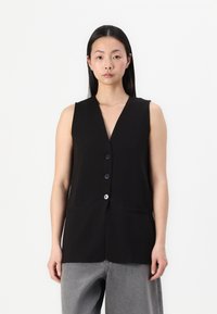 Schwarze ärmellose Weste mit V-Ausschnitt, ausgestattet mit vorderen Knöpfen und zwei Taschen, aus einem glatten Stoff mit matter Textur.