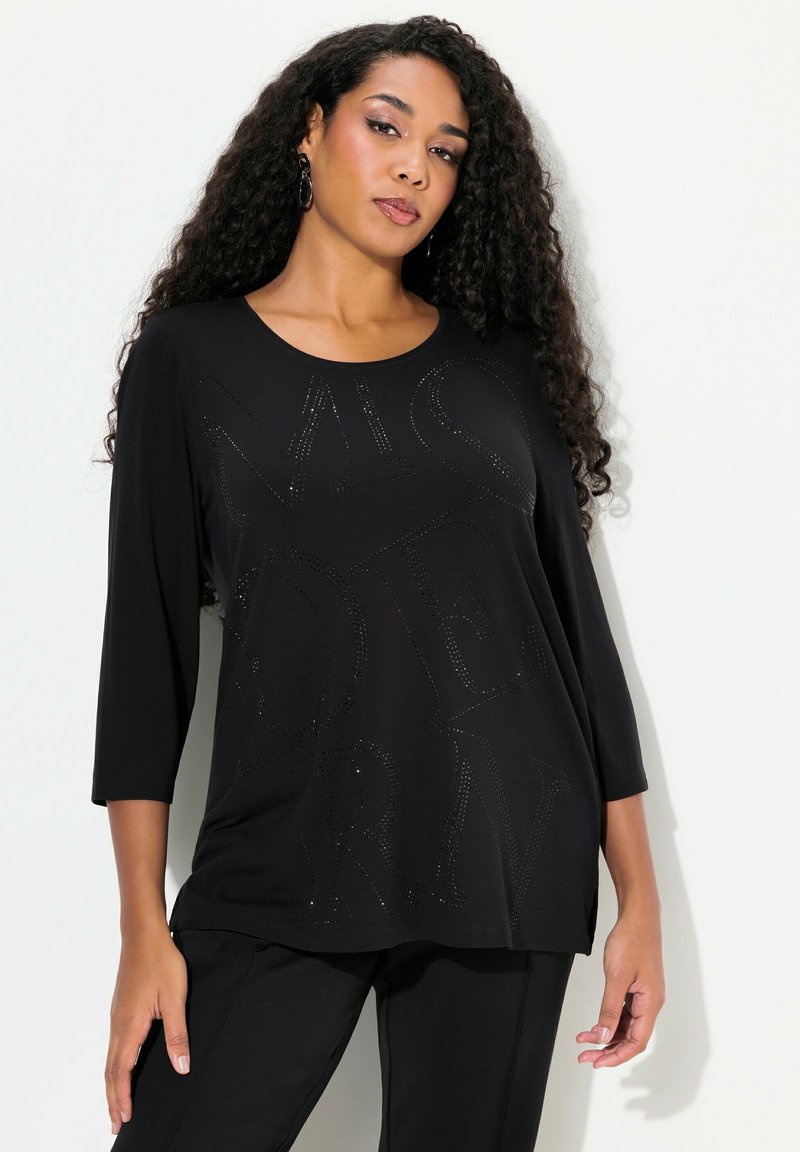 Musta pitkähihaine paita pyöreällä kaula-aukolla, jossa on teksturoitu, kimalteleva "MODERN" -design kirjaimilla edessä. Pehmeä kangas.