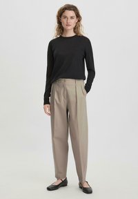 Zwarte langekousen trui gecombineerd met beige geplooide broeken. De schoenen zijn zwarte ballerina's. De stof lijkt soepel en lichtgewicht.