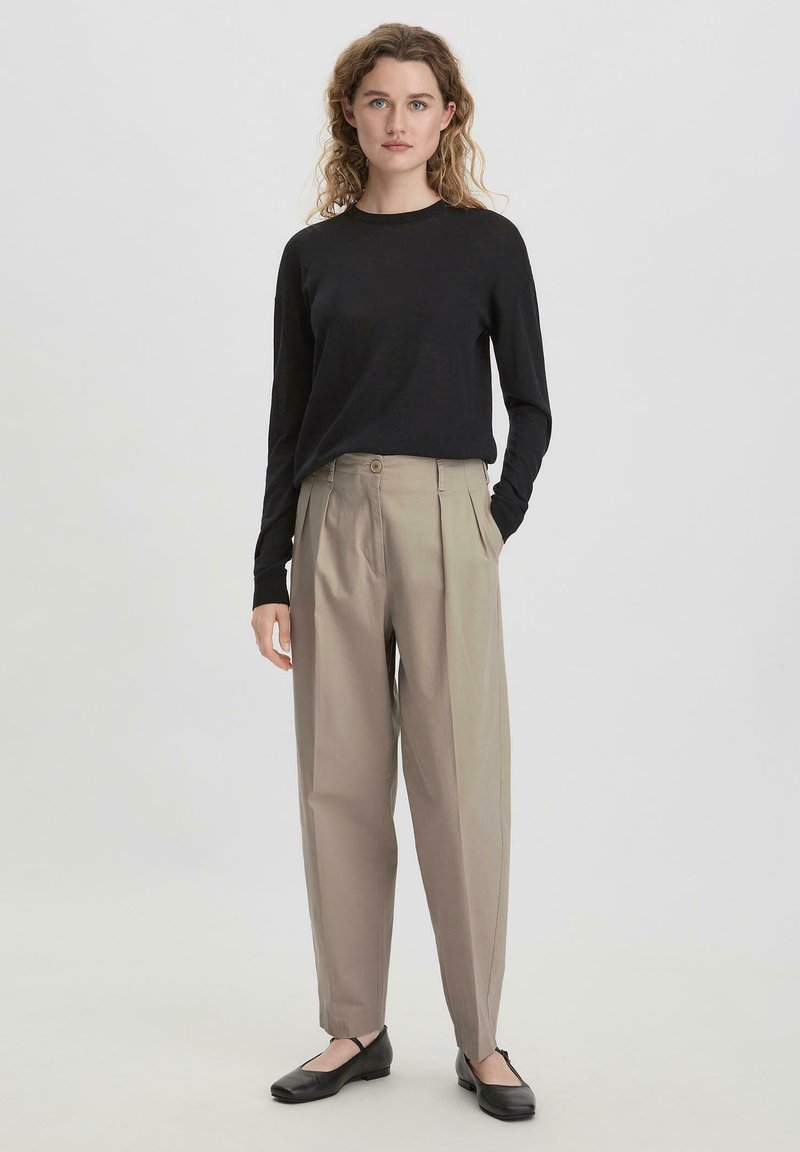 Zwarte langekousen trui gecombineerd met beige geplooide broeken. De schoenen zijn zwarte ballerina's. De stof lijkt soepel en lichtgewicht.