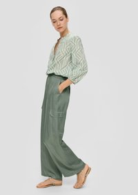 Lichtgroen blouse met patroon en een V-hals, gecombineerd met brede, effen groene broeken met zijzakken. Gedeeltelijk gedragen met sandalen met bandjes.