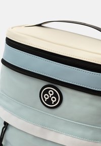 Mjuk ryggsäck med en ljusblå nylonutsida, vit rand, handtag ovanpå och en svart dragkedja. Har en cirkulär logotyp som accent.