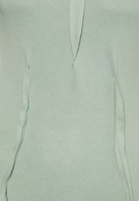 Světle zelený svetr s hladkou texturou, postranními rozparky a volným střihem z měkké látky. Bez viditelných log nebo ozdob.