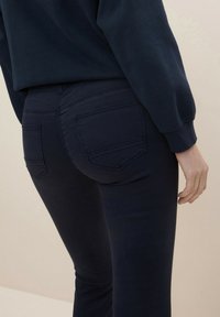 Navy blue stretch denim jeans with a mid-rise fit, featuring two back pockets and a smooth texture. Pairing with a dark sweatshirt.