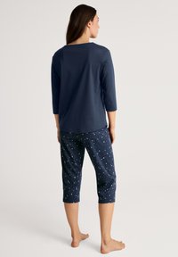 Marineblauwe katoenen shirt met driekwartmouwen, gecombineerd met gestreepte marineblauwe capri-broeken met witte sterdesigns. Zacht, casual fit.