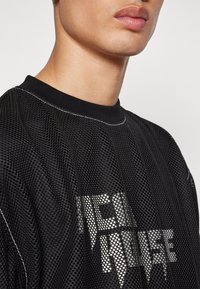 Svart mesh jersey med rund halsringning. Har reflekterande texten "ICEHOUSE" på framsidan. Mjuk textur med synliga sömnadsdetaljer.