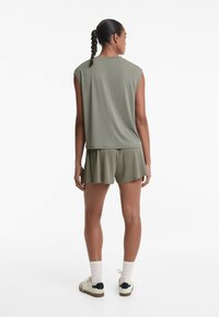 Olivgrön ärmlös topp med avslappnad passform, kombinerad med matchande shorts. Slät textur, enkel design och sidstickningsdetaljer.