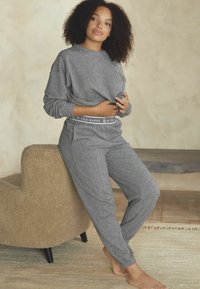 Cet ensemble de détente côtelé gris comprend un haut à manches longues et un pantalon assorti, avec une texture douce et une taille élastique.