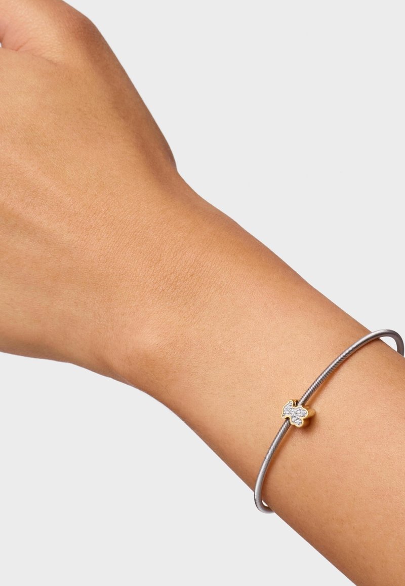 Bracciale d'argento con un accento dorato a forma di osso per cani, caratterizzato da un motivo decorativo di piccole pietre chiare. Indossato su un polso.