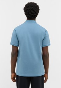 Niebieska koszulka polo wykonana z mieszanki bawełny, z klasycznym kołnierzykiem, krótkimi rękawami i gładką fakturą. Brak widocznych wzorów lub akcentów.