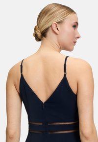 Robe bleu marine avec un décolleté en V profond dans le dos, des fines bretelles réglables et des accents en filet transparent à la taille, dotée d'une fermeture à glissière dissimulée.