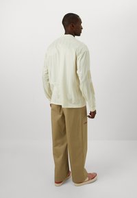 Long-sleeve cream shirt with a textured pattern, paired with light beige wide-leg pants and pink sneakers. Back view of the outfit.