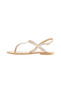Beige flache Sandalen mit T-Bar-Design und gekreuzten Riemen. Aus glattem Leder mit einer hellen Sohle und minimaler Hardware gefertigt.