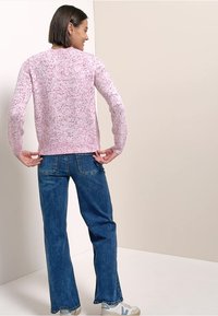 Pull en tricot rose clair à manches longues avec un motif moucheté, associé à un jean bleu évasé et des baskets blanches. Vue de dos présentée.