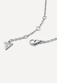Collana in argento con pendente triangolare inciso con "GUESS?", chiusa con un moschettone, che presenta una finitura lucida.