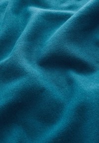 Tessuto turchese con una texture morbida e liscia, che mostra sottili variazioni di colore e superficie. Il materiale appare uniforme in tutta l'immagine.