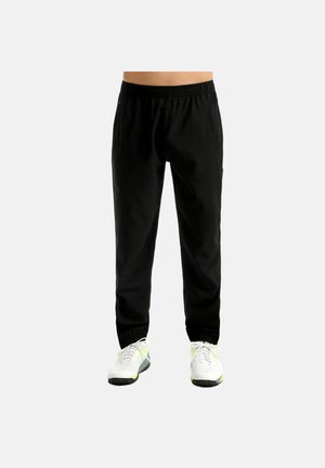 Pantalon de survêtement noir à taille et chevilles élastiques porté avec des chaussures de sport blanches et vert néon, présenté de la taille aux pieds sur un fond uni.