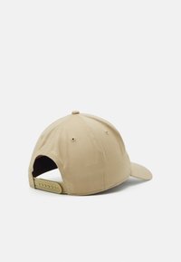 Beige cap with a curved brim, adjustable plastic strap at the back, and textured fabric. Features ventilation eyelets and a top button.