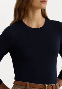 Maglione a maglia blu navy con scollatura rotonda e maniche a trequarti, caratterizzato da una texture liscia e un design aderente. Cintura marrone visibile in vita.