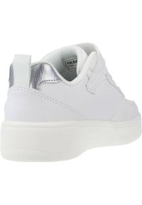 Witte sneaker met een gestructureerd lederen ontwerp, zilveren accenten op de hiel en een witte rubberen zool. Klittenbandsluiting voor gemakkelijk aan- en uitrekken.