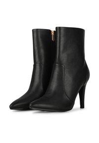 Botas de tobillo de cuero negro con punta afilada, tacón alto y cremallera lateral con un tirador dorado. Textura suave y diseño elegante.