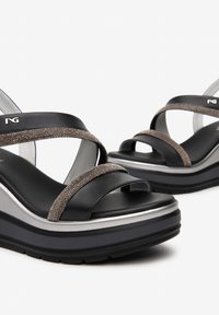 Black and silver platform sandals with crossed straps in textured fabric. Features a cushioned black sole and metallic accents.