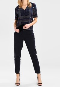 Top de rayas marinas con mangas cortas y escote en V, combinado con pantalones negros ajustados y tacones negros con tiras, sosteniendo un clutch negro.