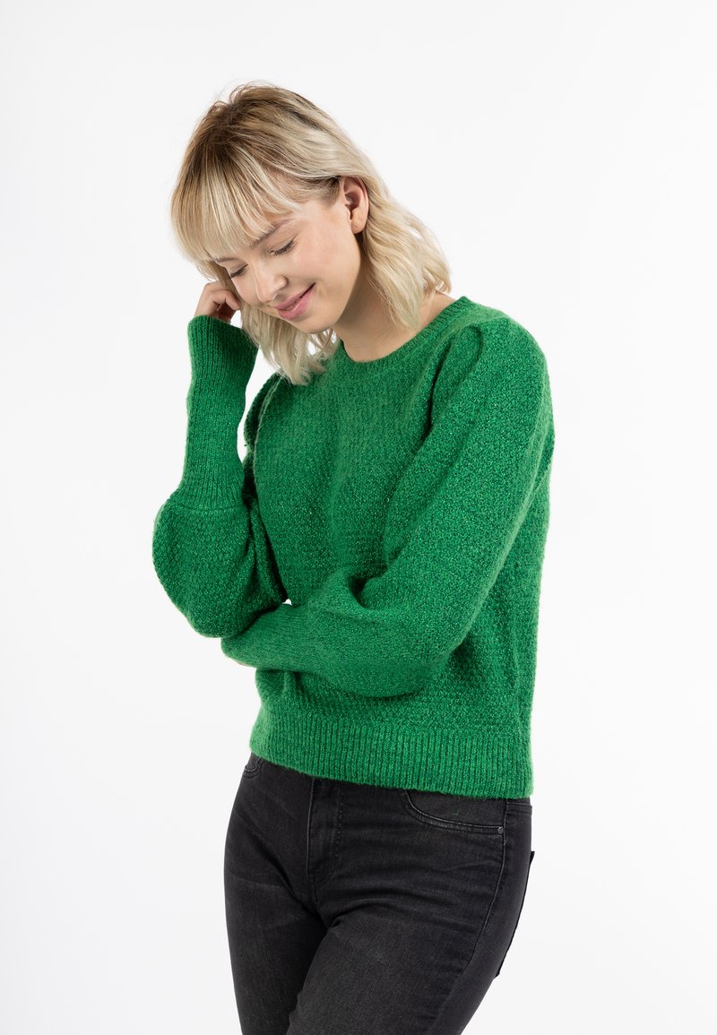 Maglione verde lavorato a maglia con finitura testurizzata, maniche lunghe e orlo a costine. Abbinato a jeans scuri.