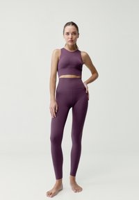 Fioletowy zestaw sportowy składający się z krótkiego topu z teksturowanym wykończeniem oraz legginsów z wysokim stanem i widocznymi szwami, noszony na boso.