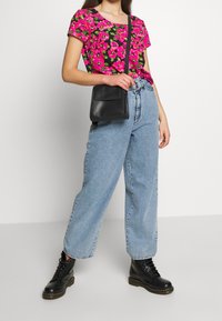 T-shirt w kwiatowy wzór w odcieniach różu i zieleni, luźne niebieskie dżinsy, czarna torebka na ramię oraz czarne sznurowane botki z grubą podeszwą.