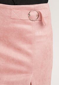 Jupe rose en suédine synthétique avec un accent de métal arrondi à la taille, dotée d'une fente latérale et d'un détail de panneau cousu.