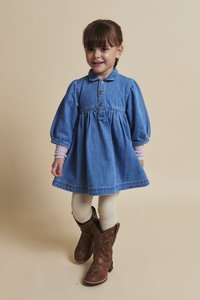 Denima kleita ar puff piedurknēm, apkakli un pogu aizdari. Brūni kovboju zābaki ar dekoratīvām šuvēm. Balti adīti legingi.