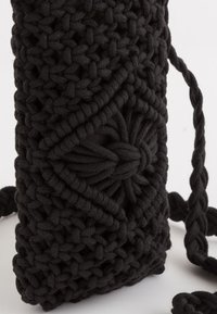 Black crochet bag featuring textured patterns, intricate knotted designs, and a braided strap, made from soft, thick yarn.