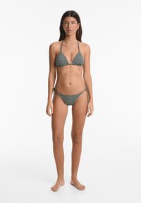 Bikini-Set mit triangulärem Oberteil und verstellbaren Bändern. Schwarz-weißer gepunkteter Stoff, aus elastischem Material gefertigt, mit glatter Textur.