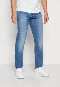 Vaqueros de mezclilla azul claro con diseño de pierna recta, que presentan un desvanecido sutil y el clásico estilo de cinco bolsillos. Combinados con zapatillas blancas.