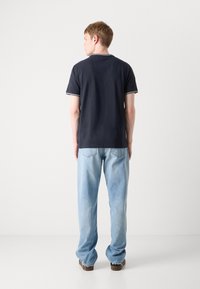 Tamsiai mėlynas medvilninis marškinėlis su baltais apykaklės ir rankovių apvadu, derinamas su šviesiai mėlynomis džinsinėmis kelnėmis, stovintis ant balto fono.