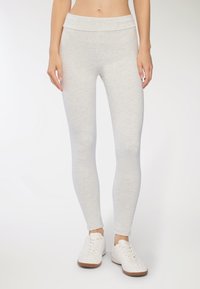 Jasnoszare legginsy wykonane z miękkiego, elastycznego materiału z szerokim pasem, dopasowanym krojem i gładką fakturą. Noszone z białymi sneakersami.