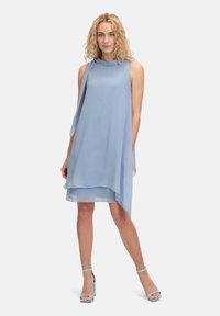 Lichtblauwe mouwloze jurk met een watervalhals en asymmetrische zoom. Gemaakt van een vloeiende stof met een gladde textuur. Gecombineerd met bijpassende hakken.