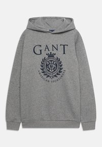 Felpa grigia in morbido tessuto con un grande logo GANT blu navy e una grafica a forma di corona sul davanti. Include una tasca a marsupio.