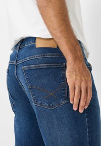 Jeans in denim blu scuro con una patch in pelle del marchio, design a cinque tasche e cuciture dettagliate sulle tasche posteriori.