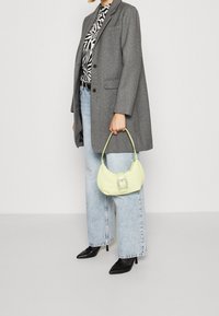 Blazer gris de espiga, superior con patrón en blanco y negro, jeans de pierna ancha en azul claro y un bolso amarillo con una hebilla cuadrada de joya. Tacones negros.