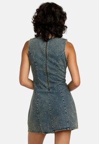 Denim-mekko on muotoiltu, siinä on hihattomat leikkaukset, takavetoketju sekä vaaleansininen pesu, jossa näkyvät saumat ja ompeleet.