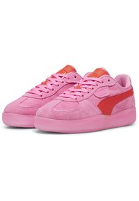 Sneaker in suede rosa con una suola rosa liscia, caratterizzate da una striscia rossa e dettagli accentati. I lacci e la linguetta sono anch'essi rosa, con dettagli del logo sul lato.