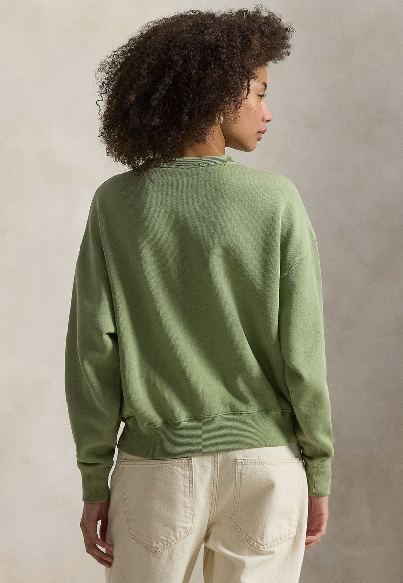 Green, oversized sweatshirt made of textured material with a round neckline and ribbed cuffs, paired with light beige pants.