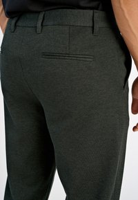 Mørkegrå skreddersydde bukser laget av teksturert stoff, med en innfelt lomme på baksiden og en glatt midjebånd.