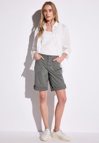 Shorts gris légers enroulés avec poches avant, associés à un débardeur blanc et une chemise boutonnée en lin blanc. Baskets décontractées.