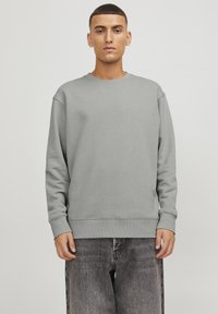 Sudadera gris de tejido texturizado, con cuello redondo y mangas largas. Combinada con unos vaqueros negros de corte holgado.
