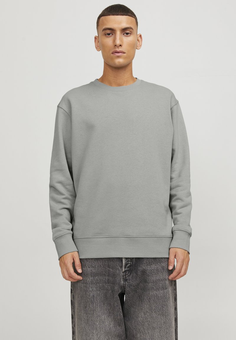 Sudadera gris de tejido texturizado, con cuello redondo y mangas largas. Combinada con unos vaqueros negros de corte holgado.