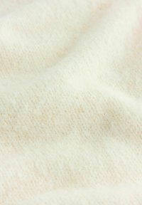 Tissu en maille de couleur crème, doux, présentant un motif texturé avec un léger éclat, créant une surface lisse et accueillante.