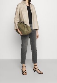 Beżowa skórzana kurtka na zatrzaski, czarna bluzka, szare dżinsy, zielona torebka oraz czarne sandały na obcasie z cienkimi paskami.